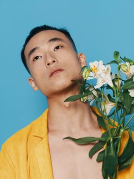 A guy with a bouquet of white flowers looks up on a blue background and a yellow coat. High quality photo