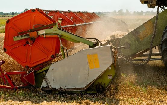 Platform grain header with thresher reel, cutter bar reaping cereal ears. Rotary straw walker combine harvester cuts and threshes ripe wheat grain. Gathering crop by agricultural machinery on field