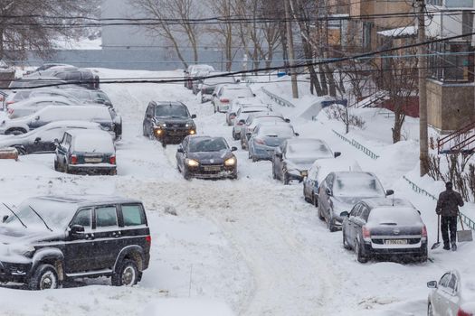 Tula, Russia - February 13, 2021: Two cars drive through a snowy yard between rows of parked cars in deep snow.