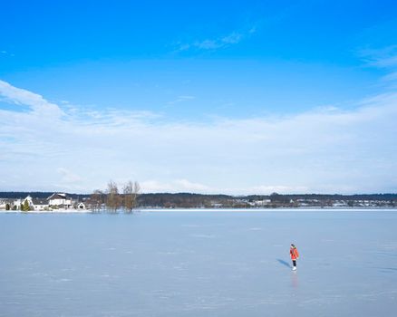 Elst, Netherlands, 10 february 2021: girl in red coat skates on ice of flood planes near river rhine near Rhenen in the centre of the netherlands