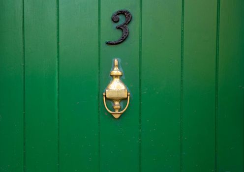 House number 3, green wooden front door with gold brass metal door knocker. Old antique painted door with knocker. UK, Suffolk