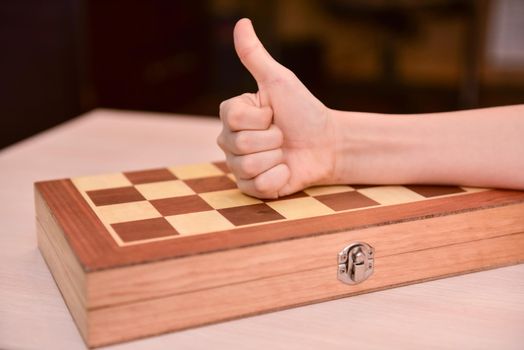 child's hand on the chessboard showing thumb up. cool game at home.