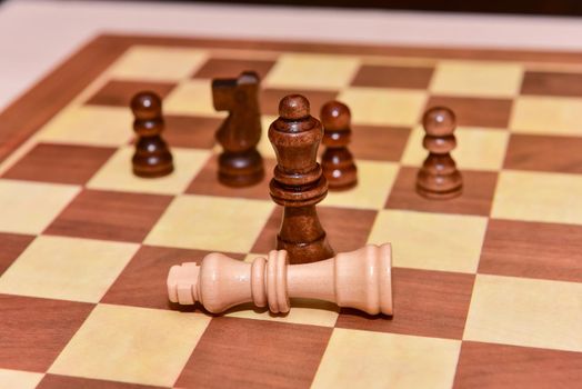 wood chess pieces on board game. brown vintage background. checkmate. the king is defeated by the queen.