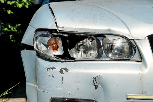 Close-up of a broken headlight on a gray car on a sunny day. Crash concept.