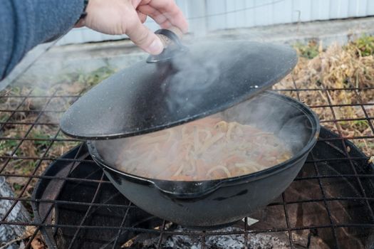 Cooked food a campfire on a camping trip. Camp kitchen, cooking food in the forest on fire. Frying pan on fire. rustic grill for cooking pilaf.