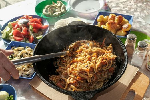 Seafood pilaf in an old cast iron cauldron. table with vegetable dishes.