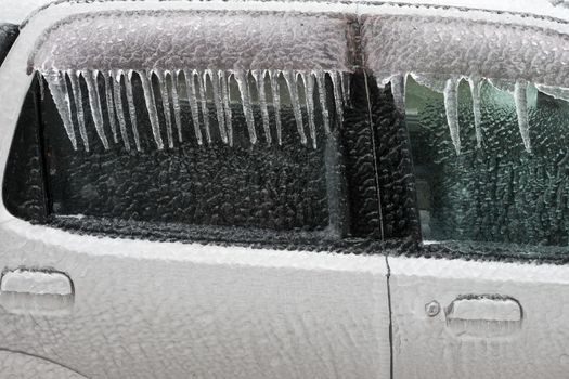 Ice covered car window close up. Car covered with ice and icicles after freezing rain. Bad frosty weather, ice storm.