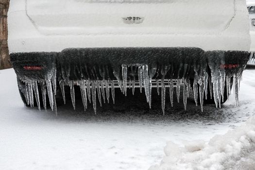 Ice-covered car bumper with icicles close up, vehicle parking safety after freezing rain in Europe.