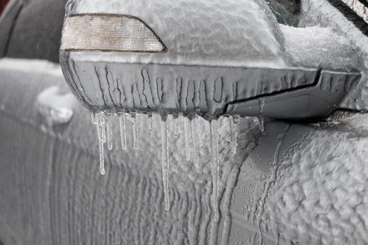 Frozen rearview mirror and wiper of the car with icicles, ice and frost.