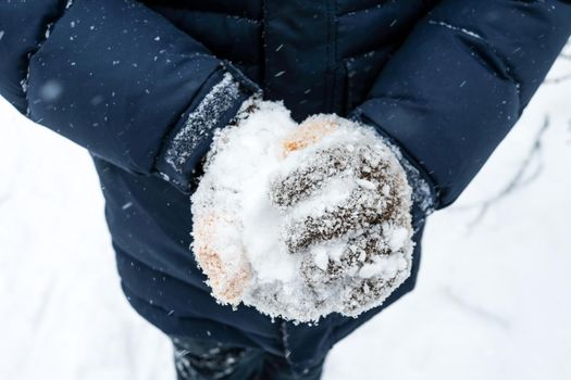 close up gloved hands make a snowball.