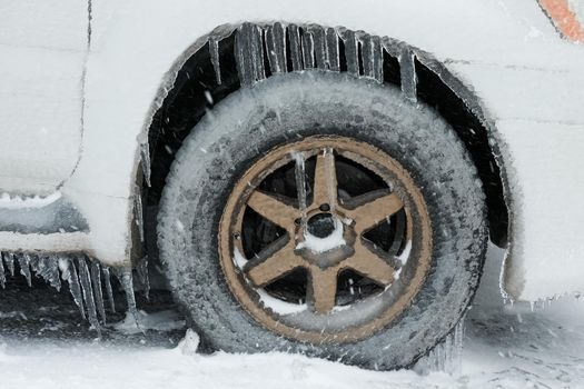 Ice buildup and icicles on a car and close-up of a frozen wheel.