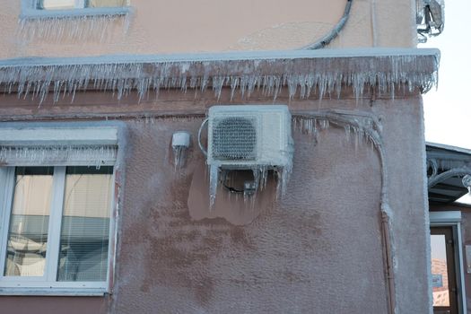 air conditioner on building, walls and windows of the building are covered with ice and icicles.