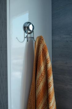 chrome hook-hanger on tiles with hanging towel in bathroom close-up.