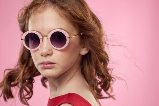 girl with curly hair sunglasses childhood joy pink background. High quality photo