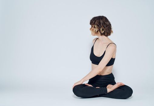 A woman in leggings sits cross-legged on the floor and turns to the sides. High quality photo