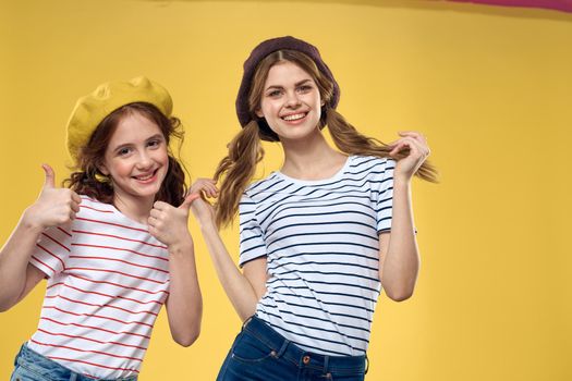 Cheerful sisters in hats striped T-shirts joy lifestyle yellow background family. High quality photo