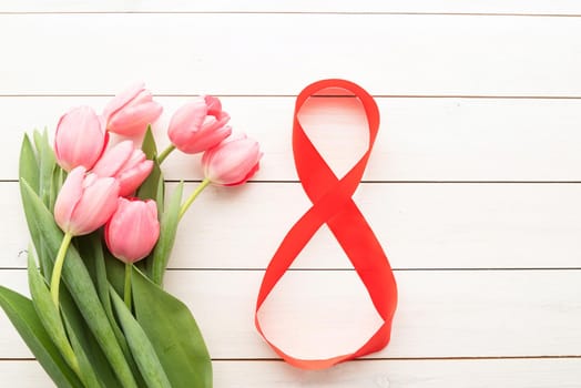 pink tulips and red number eight for international womens day over white wooden table background with copy space