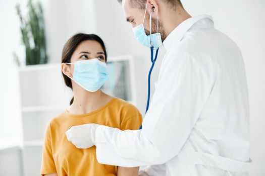 doctor with a stethoscope listens to the heartbeat of a patient wearing a medical mask. High quality photo