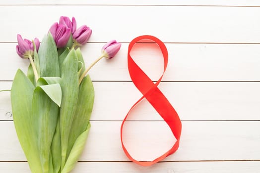 Purple tulips and red number eight for international womens day over white wooden table background with copy space