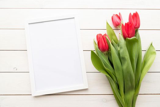 White frame with spring tulips top view over white wooden background. Mock up design.