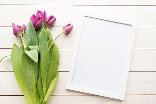 White frame with purple spring tulips top view over white wooden background. Mock up design.