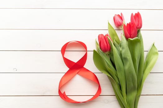 Red tulips and red number eight for international womens day over white wooden table background with copy space