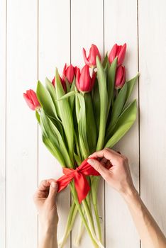 Woman hands making a bouquet of spring tulips on white wooden table top view flat lay