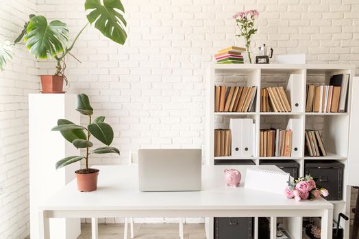 Cozy home interior. Stylish cozy workspace with laptop, bookshelves and plants