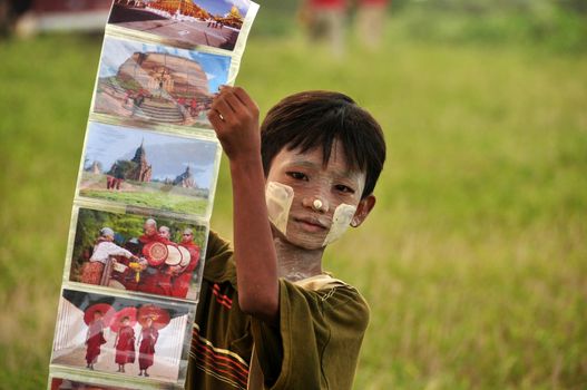 BAGAN, MYANMAR - NOVEMBER 18, 2015: Little ethnic boy showing colorful photos, Cute Asian boy with face paint in tanaka showing collage of colorful photos of oriental culture. Traditional look