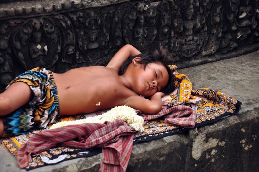 ANGKOR, CAMBODIA - AUG 28, 2013: Sleeping ethnic boy on step of temple, Little ethnic boy sleeping on ornamental rug on stone step of ancient Angkor Wat temple. Mowgli