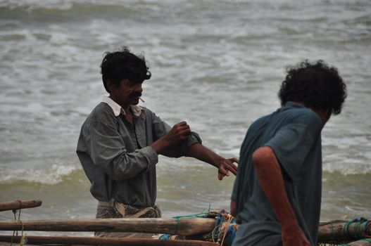 HIKKADUWA, SRI LANKA - 18 DECEMBER 2011 Group of ethnic men near wooden authentic boat close to rough ocean waves. Fishermen life