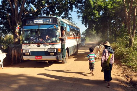 BAGAN, MYANMAR - NOVEMBER 18, 2015: Bus on rural road in village, View of people and cattle on remote rural road with bus under green trees. Mingalazedi Sulamani Shwezigon Ananda Htilominlo