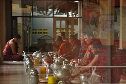 NAKHONSITHAMMARAT, THAILAND - JUNE 7, 2014: Group of monks at table durind. View of men in red robes of monks sitting at table with utensils having meal.