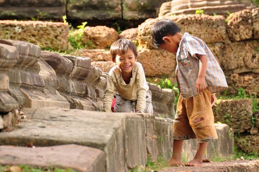 ANGKOR, CAMBODIA - AUG 28, 2013: Cheerful ethnic kids on stone fence, Little Asian boys spending time together on stone fence of ancient temple of Angkor Wat