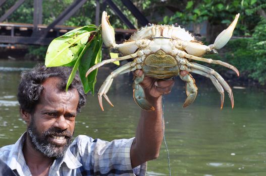 HIKKADUWA, SRI LANKA - 18 DECEMBER 2011 Adult bearded ethnic fisherman with huge caught crab outdoors looking away. Bearded man holding caught crab