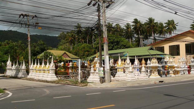 KOH SAMUI ISLAND, THAILAND - 24 JUNE 2019 Deserted road with spirit houses in Thai style. Typical countryside road with shop of wooden spirit houses on roadside on cloudy sky background before storm.