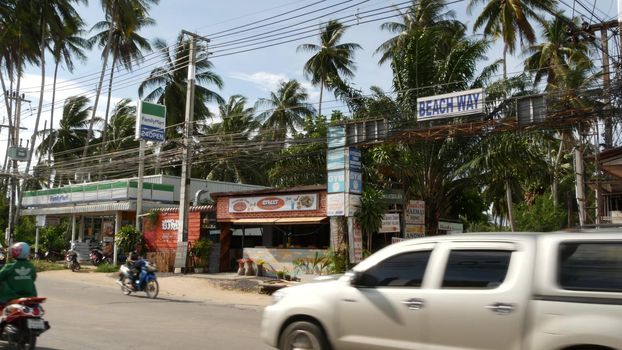 KOH SAMUI ISLAND, THAILAND - 24 JUNE 2019 Driving cars and small shops on roadside. Beach way and chain store Family mart on main road. Typical touristic village street. Thai people on motorbikes