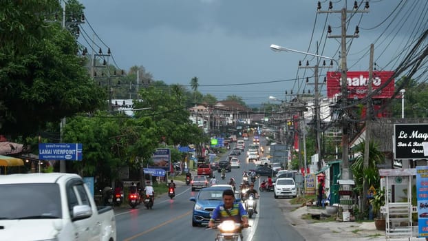 KOH SAMUI ISLAND, THAILAND - 11 JULY 2019 Busy transport populated city street in cloudy day. Typical street full of motorcycles and cars. Thick blue clouds before storm during wet season