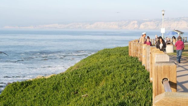 La Jolla, San Diego, CA USA -24 JAN 2020: Group of people walking on steep high cliff promenade, multiethnic pedestrians, tourists during holidays. Succulents and ocean, golden sunset in California.