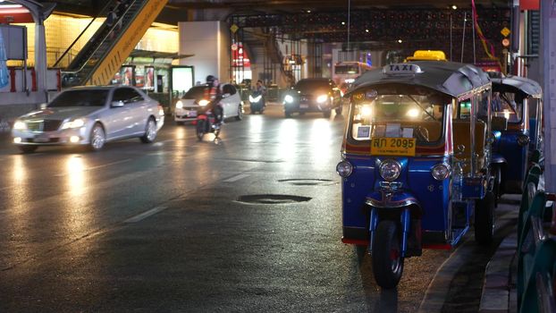 BANGKOK, THAILAND - 18 DECEMBER, 2018: Traditional Thai taxi - Tuk Tuk awaits tourists along the road. Night traffic of overpopulated city. Symbol of asian country, unique vehicle.