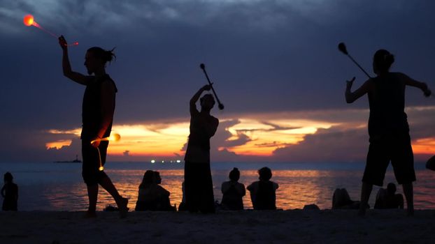 PHANGAN, THAILAND - 23 MARCH 2019 Zen Beach. Silhouettes of performers on beach during sunset. Silhouettes of young anonymous entertainers rehearsing on sandy beach against calm sea and sundown sky