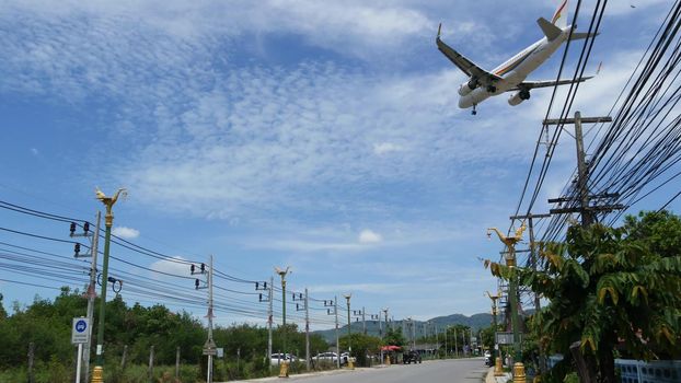 KOH SAMUI ISLAND, THAILAND - 23 JUNE 2019 Plane landing over typical main road street of tropical town. Aircraft flying to Bangkok airways airport, exotic touristic resort. Thai people on motorbikes