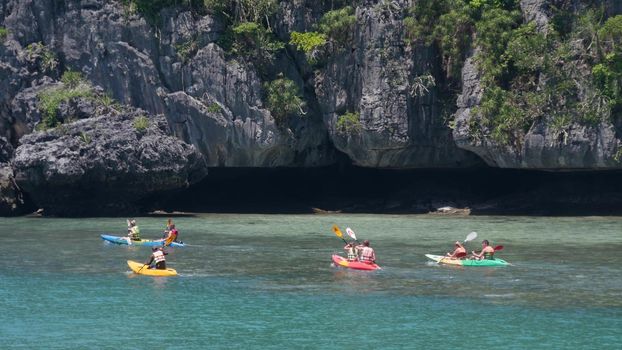 ANG THONG MARINE PARK, SAMUI, THAILAND - 9 JUNE 2019: People kayaking near cliff in paradise sea. Group of tourists paddling while riding kayaks on blue Idyllic turquoise ocean water near rocks