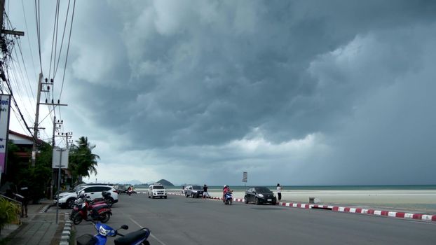 KOH SAMUI ISLAND, THAILAND - 14 JULY 2019 Gloomy landscape of seafront with cars and people awaiting hurricane. Motorbikes riding on asphalt road under amazing heavy clouds in Nathon city