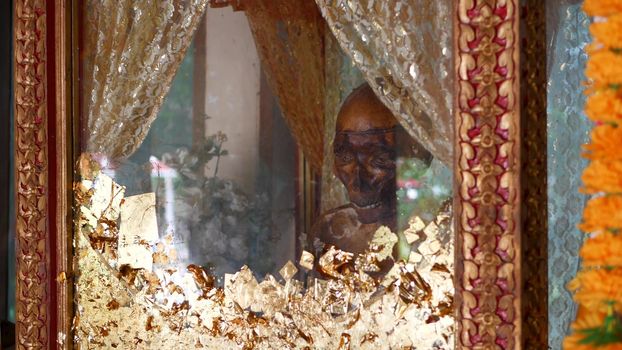 KOH SAMUI ISLAND, THAILAND - 17 JULY 2019: Wat Khiri Wongkaram Buddhist Temple. The mummified body of monk and gold leaf. Exotic tradition of storing the relics of saints who died during meditation