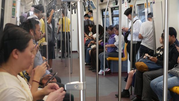 BANGKOK, THAILAND - 10 JULY, 2019: Asian passengers in train using smartphones. Thai people online surfing internet in bts car. Public transportation. Addiction from social media and phone in subway
