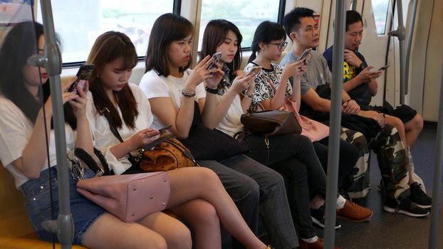 BANGKOK, THAILAND - 13 JULY, 2019: Asian passengers in train using smartphones. Thai people online surfing internet in bts car. Public transportation. Addiction from social media and phone in subway