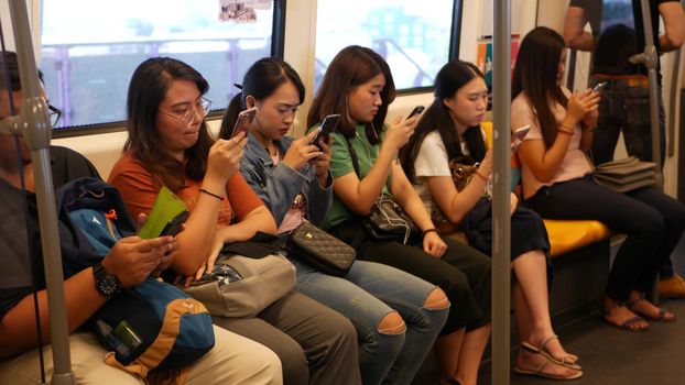 BANGKOK, THAILAND - 13 JULY, 2019: Asian passengers in train using smartphones. Thai people online surfing internet in bts car. Public transportation. Addiction from social media and phone in subway
