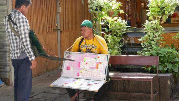 BANGKOK, THAILAND - 13 JULY 2019: Lat Mayom floating market. Lottery ticket sellers on city street. Ethnic men selling traditional tickets and talking with each other on city street.