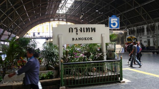 BANGKOK, THAILAND - 11 JULY, 2019: Signpost with name of city. Hua Lamphong main railroad station of state railway transport, SRT. Passengers on platform near sign board. People and trains on tracks